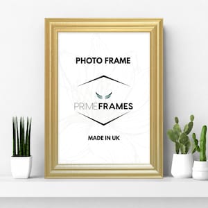 May include: A rectangular gold-coloured photo frame with a textured border. The white insert features the black text PHOTO FRAME, the logo PRIME FRAMES with a small wing icon, and the text MADE IN UK centred within a thin black diamond outline.