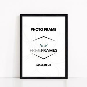 May include: A rectangular black photo frame with a white insert featuring the black text PHOTO FRAME, the logo PRIME FRAMES with a small wing icon, and the text MADE IN UK. The background of the insert displays a faint, light grey floral line drawing.