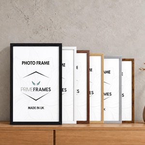May include: A collection of six rectangular photo frames in various finishes including black, white, dark brown, light wood, silver, and rustic brown. Each frame contains a white insert with the text PHOTO FRAME, PRIMEFRAMES, and MADE IN UK.