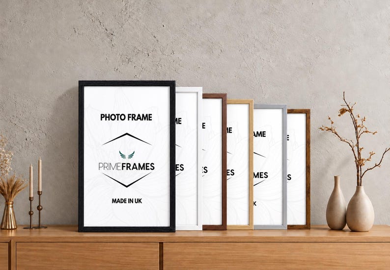 May include: A collection of six rectangular photo frames in various finishes including black, white, dark brown, light wood, silver, and rustic brown. Each frame contains a white insert with the text PHOTO FRAME, PRIMEFRAMES, and MADE IN UK.