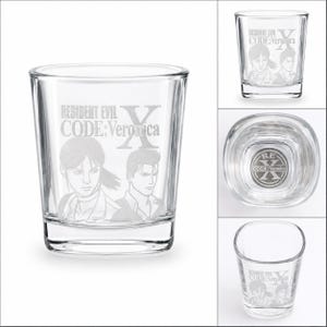 May include: A clear glass shot glass featuring an etched design of the Resident Evil Code: Veronica X logo and two characters. The base of the glass includes a circular emblem with the text RE Code: Veronica X engraved on the interior bottom surface.