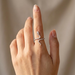 Peut inclure: Une bague serpent argentée au design enroulé qui entoure le doigt. La surface du serpent est incrustée de petites pierres claires et scintillantes qui recouvrent toute la longueur du corps, de la tête jusqu'à la pointe de la queue.