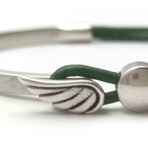 May include: A silver bracelet with a green leather band. The bracelet features a wing charm and a round silver bead. The design is simple and elegant, suitable for everyday wear.