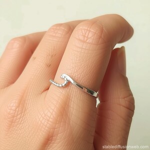 Puede incluir: Un anillo plateado con un diseño de ola. El anillo presenta una banda curva y una parte superior en forma de ola con pequeños adornos redondos. El anillo se lleva en un dedo.