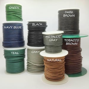 May include: Spools of leather cord in various colors, including green, navy blue, black, metallic gray, and natural. Each spool is labeled with its color name. The cords are tightly wound and ready for crafting projects.