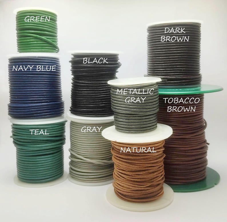May include: Spools of leather cord in various colors, including green, navy blue, black, metallic gray, and natural. Each spool is labeled with its color name. The cords are tightly wound and ready for crafting projects.
