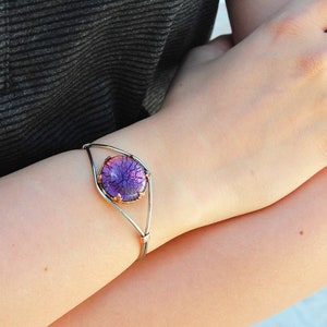 May include: A silver bangle bracelet with a purple and pink glass cabochon set in a copper frame.