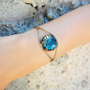 May include: A copper and silver wire bracelet featuring a blue and green glass cabochon. The cabochon has a crackled texture.