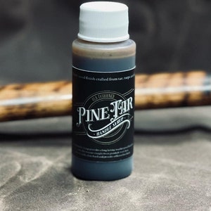 May include: A small bottle of Pine Tar Handle Syrup with a white cap and a black label. The label features the text "Pine Tar Handle Syrup" in a vintage font. The bottle is filled with a dark brown liquid.