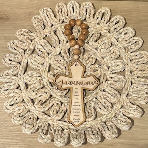 May include: A wooden cross with the name "Giovanni" engraved on it. The cross is decorated with a beaded rosary and a quote from Psalm 139:14: "You are wonderfully made."