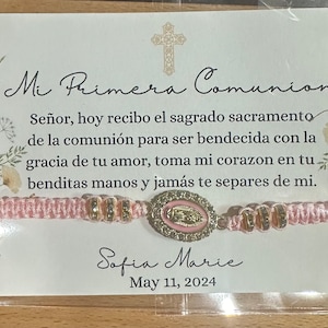 May include: A pink and gold bracelet with a religious charm. The bracelet has the text "Mi Primera Comunion" and "Sofia Marie" with the date "May 11, 2024".