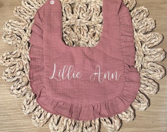 May include: A pink ruffled bib with the name "Lillie Ann" embroidered in white.