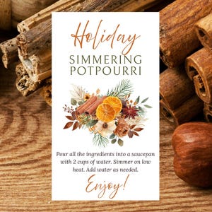 May include: A white card with the text "Holiday Simmering Potpourri" and instructions, surrounded by cinnamon sticks, dried orange slices, and floral elements. The background is a wooden surface.