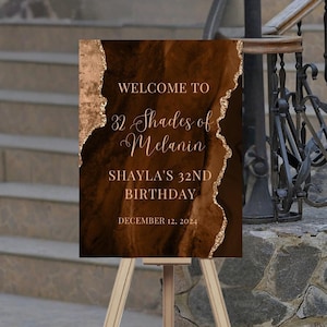 May include: Welcome to 32 Shades of Melanin, Shayla's 32nd Birthday, December 12, 2024. A brown and gold birthday sign with a marble-like design.