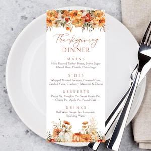 May include: A Thanksgiving Dinner menu card with floral accents, placed on a white plate with silverware and a napkin. The menu lists mains like turkey breast and ham, sides like mashed potatoes, desserts like pumpkin pie, and drinks.