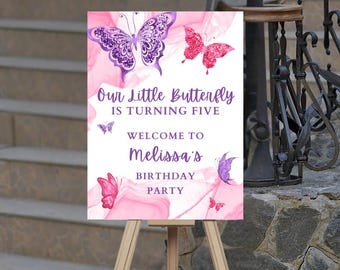 May include: A pink and white sign with purple and pink butterflies. The sign reads "Our Little Butterfly is Turning Five. Welcome to Melissa's Birthday Party."