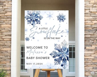 May include: A white sign with blue snowflakes and the text "A Little Snowflake is on the way" and "Welcome to Melissa's Baby Shower Nov 17, 2024". The sign is on a wooden easel.