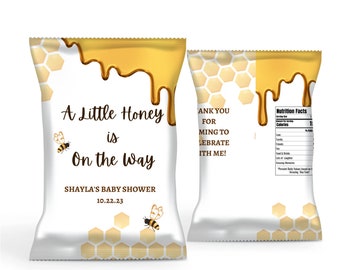 May include: A white favor bag with a honeybee theme. The bag has a dripping honey design and the text "A Little Honey is On the Way" with the date "10.22.23".