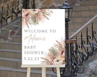 May include: A white sign with a floral design and gold lettering. The sign reads "Welcome to Melissa's Baby Shower 5.22.23".