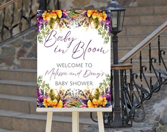 May include: A white sign with purple text that reads "Baby in Bloom" and "Welcome to Melissa and Doug's Baby Shower". The sign is decorated with watercolour flowers in shades of yellow, orange, purple, and green. The sign is on a white easel.