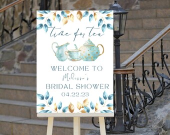 May include: A white sign with blue and gold leaves and a teapot and teacup design. The sign says "Time for Tea" and "Welcome to Melissa's Bridal Shower 04.22.23".