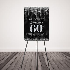 May include: A black and silver welcome sign with glitter accents. The sign reads "Welcome to Patricia's 60th Birthday Celebration August 17, 2024".