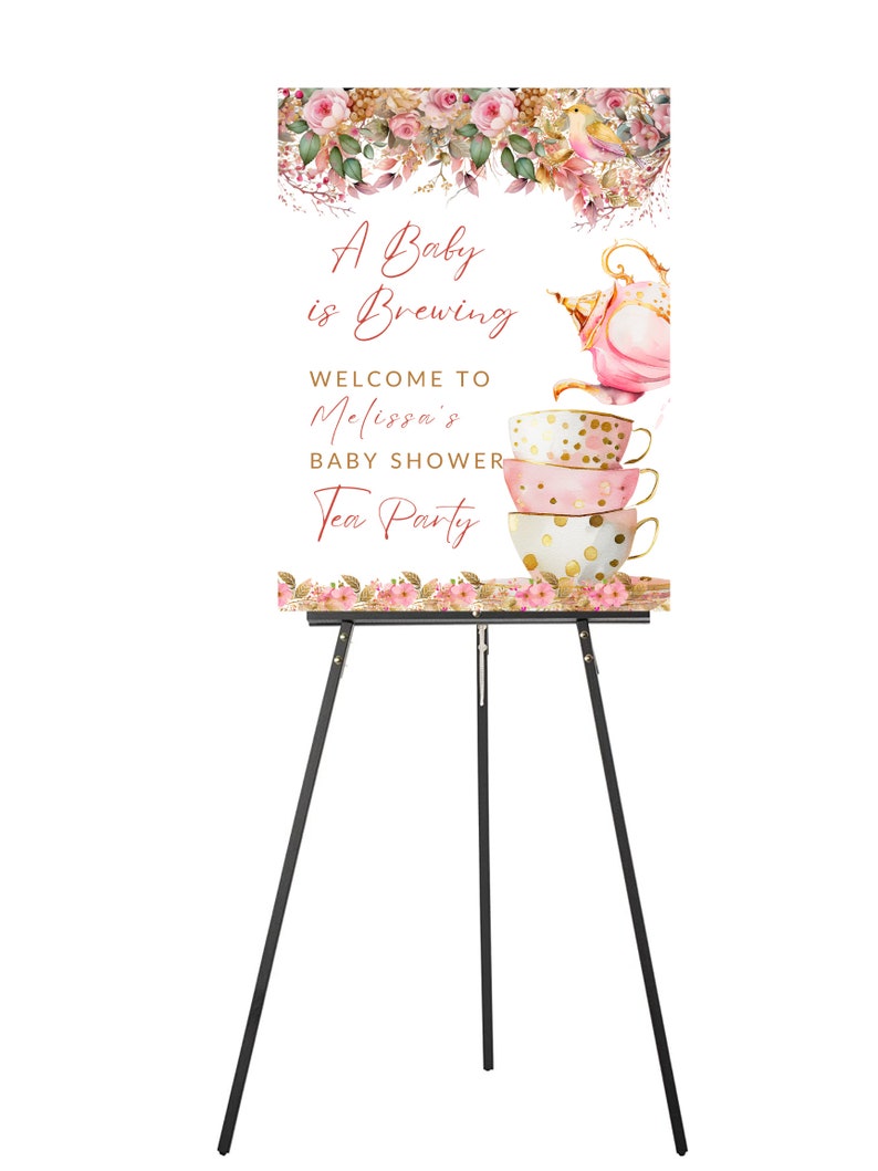 May include: A baby shower sign on a black easel. The sign has a floral design at the top and bottom. The text reads "A Baby is Brewing" and "Welcome to Melissa's Baby Shower Tea Party". The sign features a teapot and teacups.