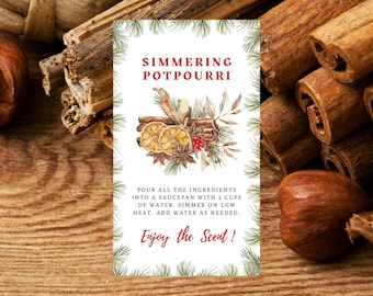 May include: A white card with green pine branches around the border. The card has the text "Simmering Potpourri" in red letters. The card also has a watercolor illustration of cinnamon sticks, orange slices, star anise, and cloves. The text below the illustration reads "Pour all the ingredients into a saucepan with 2 cups of water. Simmer on low heat. Add water as needed. Enjoy the Scent!"