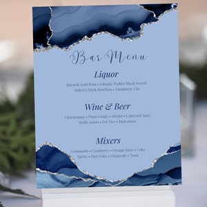 May include: A light blue bar menu card with a navy blue and silver design. The card lists liquor, wine & beer, and mixers. The text includes drink options like Bacardi Gold Rum, Chardonnay, and Lemonade. The card is displayed on a white stand.
