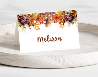 May include: A white place card with a watercolour design of autumn leaves and flowers in shades of orange, red, yellow, and brown. The name "melissa" is printed in brown text.