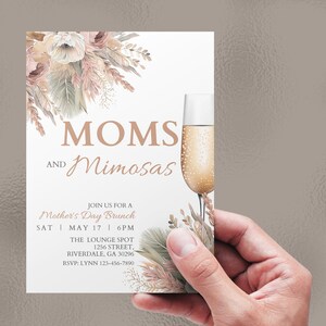 May include: A white invitation card with a floral design in shades of pink, beige, and gold. The text reads "MOMS AND Mimosas" and includes details for a Mother's Day brunch.