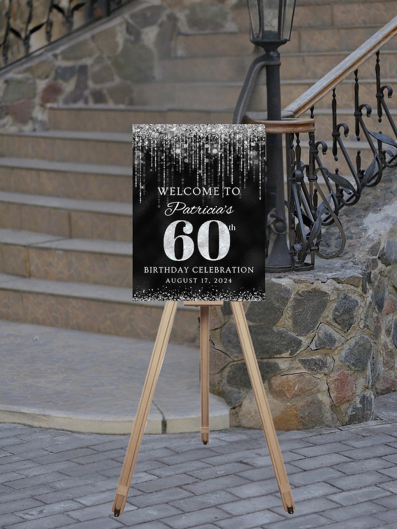 May include: Black and silver welcome sign with glitter accents. The sign reads "Welcome to Patricia's 60th Birthday Celebration August 17, 2024". The sign is on a wooden easel.