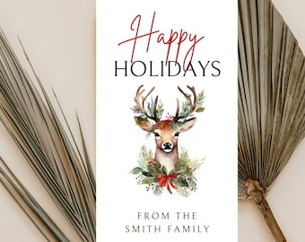Può includere: Un biglietto bianco con il testo "Happy Holidays" in rosso e nero. Un'illustrazione ad acquerello di un cervo con un fiocco rosso e fogliame verde circonda la testa del cervo. Il testo "From the Smith Family" è in fondo al biglietto.