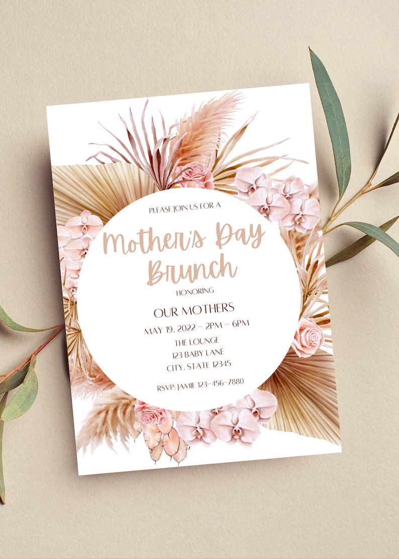May include: A white invitation with a floral design featuring pink orchids, beige pampas grass, and a circle with the text "Mother's Day Brunch" in brown lettering. The invitation includes details for a brunch honoring mothers on May 19, 2022, from 2 PM to 6 PM at The Lounge, 123 Baby Lane, City, State 12345. RSVP to Jamie at 123-456-7880.