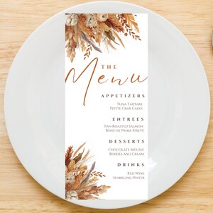 Op de afbeelding: Een witte menukaart met een bruin bloemenontwerp aan de boven- en onderkant. De tekst "The Menu" is geschreven in bruin cursief schrift. Het menu bevat voorgerechten, hoofdgerechten, desserts en dranken.