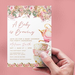 May include: A pink and gold baby shower invitation with a teapot and teacups. The invitation reads "A Baby is Brewing" and includes the date, time, and location of the event. RSVP information is also included.