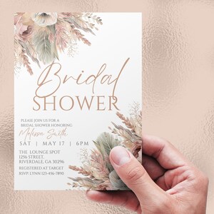 May include: A white bridal shower invitation with a floral design in shades of pink, beige, and green. The text reads "Bridal Shower" in a cursive font, followed by "Please join us for a bridal shower honoring Melissa Smith" and the date and time of the event. The invitation also includes the location, "The Lounge Spot, 1256 Street, Riverdale, GA 30296", and the registry information, "Registered at Target". The RSVP information is "RSVP: Lynn 123-456-7890".