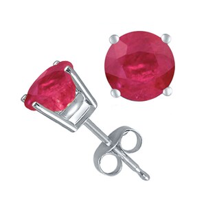 May include: A pair of stud earrings featuring round, faceted, deep red rubies set in four-prong silver-toned metal settings. One earring is shown from the front, while the other is angled to display the post and the accompanying metal backing.