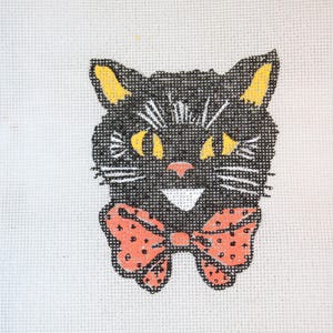May include: Black cat with yellow ears and a red polka dot bow tie. The cat has a wide smile and white whiskers.