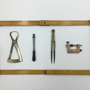 Peut inclure: Quatre outils de mesure anciens, dont un compas, un pied à coulisse, une petite pince et une tige métallique, sont présentés sur un fond de règle en bois.