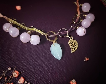 May include: A delicate necklace with pink and light blue gemstone beads, gold leaf charms, and a brown and purple braided cord.