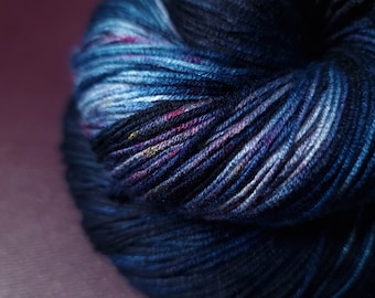 Könnte beinhalten: Eine Garnrolle in tiefem Blau mit Schattierungen von Lila und Weiß. Das Garn ist fest gewickelt und hat eine weiche, flauschige Textur.