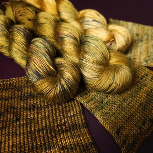 May include: A skein of golden yellow yarn with flecks of green, blue, and red. The yarn is shown with a swatch of knitted fabric in the same colourway.