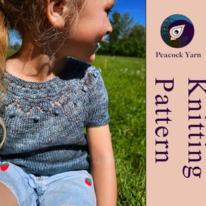 Puede incluir: Una camiseta de punto azul moteado de manga corta con cuello redondo que presenta un canes&uacute; texturizado decorativo con peque&ntilde;as borlas y detalles de encaje. El panel lateral incluye el texto Peacock Yarn y Knitting Pattern con un logo.