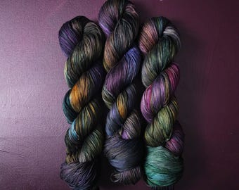 May include: Three skeins of yarn in shades of purple, green, and brown. The yarn is twisted and has a variegated colour pattern.