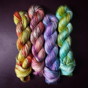 May include: Four skeins of yarn in different colours, including green, purple, pink, and yellow. The yarn is hand-dyed and has a speckled appearance.