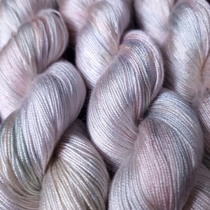 Peut inclure: Gros plan de plusieurs écheveaux de fil aux couleurs pastel douces. Le fil semble être un mélange de rose, de gris et de crème, avec de subtiles variations de couleur. La texture du fil est lisse et légèrement brillante, suggérant une fibre luxueuse. Le fil est bien enroulé.