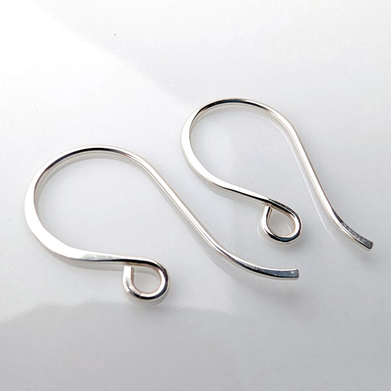 May include: Two silver-colored earring hooks. Each hook has a curved top and a small loop at the bottom. The hooks are made of a shiny, smooth metal and are set against a white background.