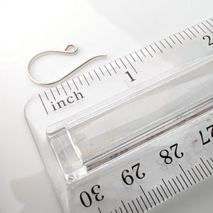 May include: A silver-colored earring hook next to a clear ruler. The ruler shows inch measurements. The earring hook is approximately 1 inch in length.
