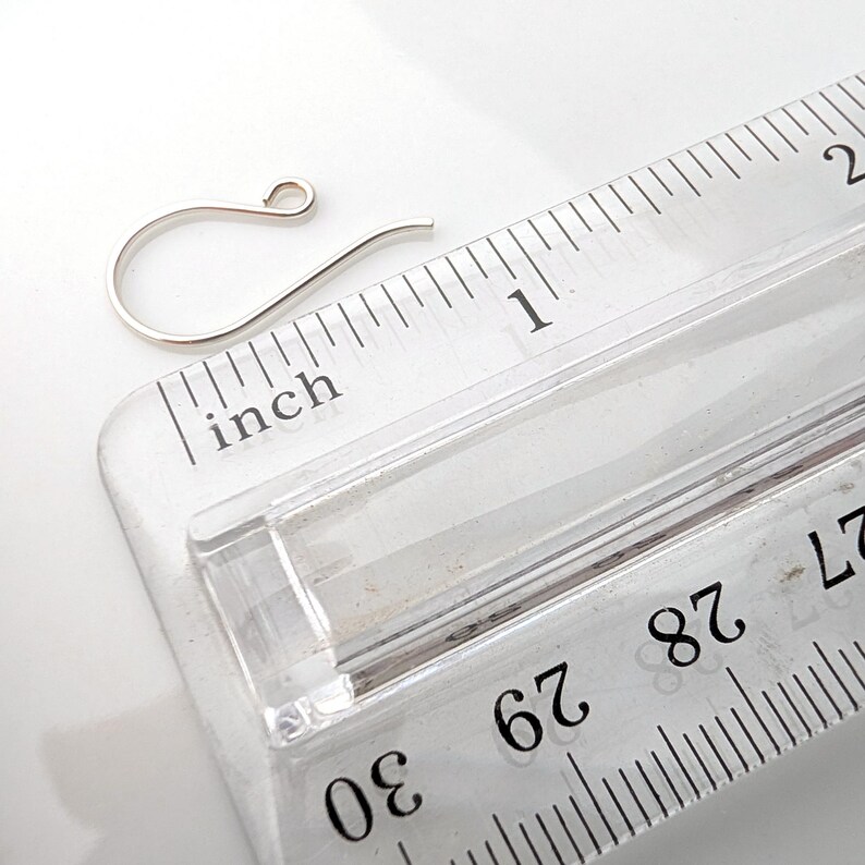 May include: A silver-colored earring hook next to a clear ruler. The ruler shows inch measurements. The earring hook is approximately 1 inch in length.